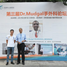 Mass General surgeon Chaitanya Mudgal, MD, right, and an attendee in front of a sign announcing Dr. Mudgal's conference in Guigang City, China.